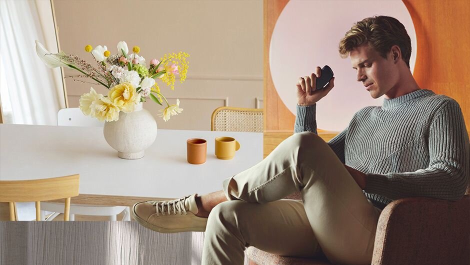 Muž sedí na židli a drží v ruce Ploom X. V pozadí je jídelní stůl s vázou a květinami.