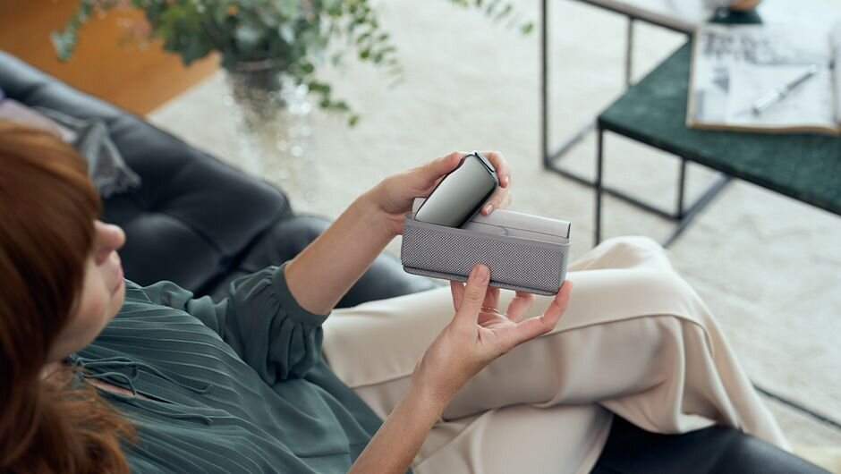 Žena sedící na pohovce se zařízením Ploom X Advanced a textilním pouzdrem Ploom