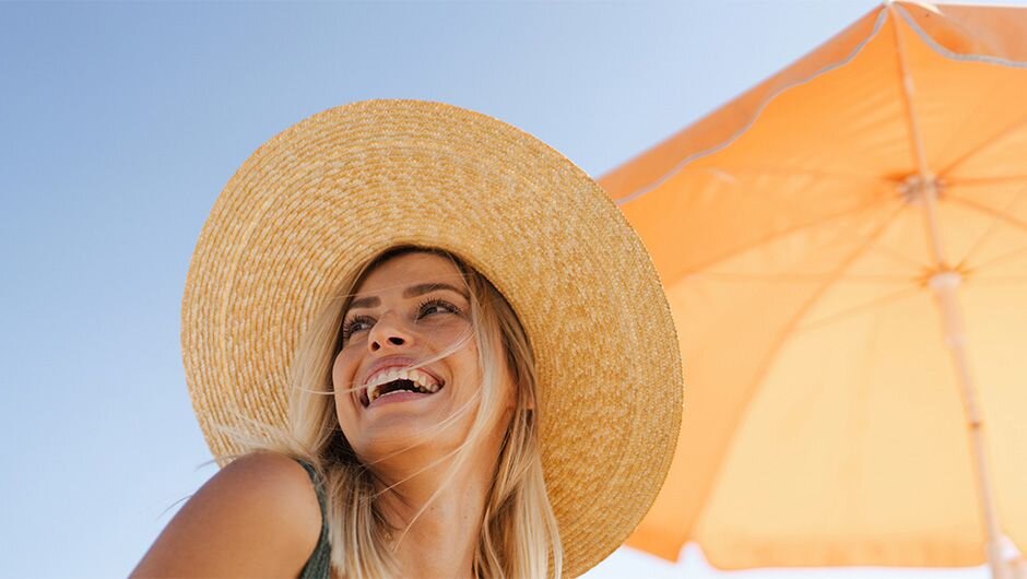 Žena v plážovém klobouku pod oranžovým slunečníkem
