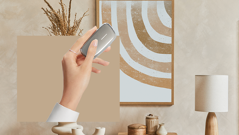 Koláž interiérových doplňků v běžovém odstínu a v popředí ženská ruka drží stříbrné zařízení Ploom X