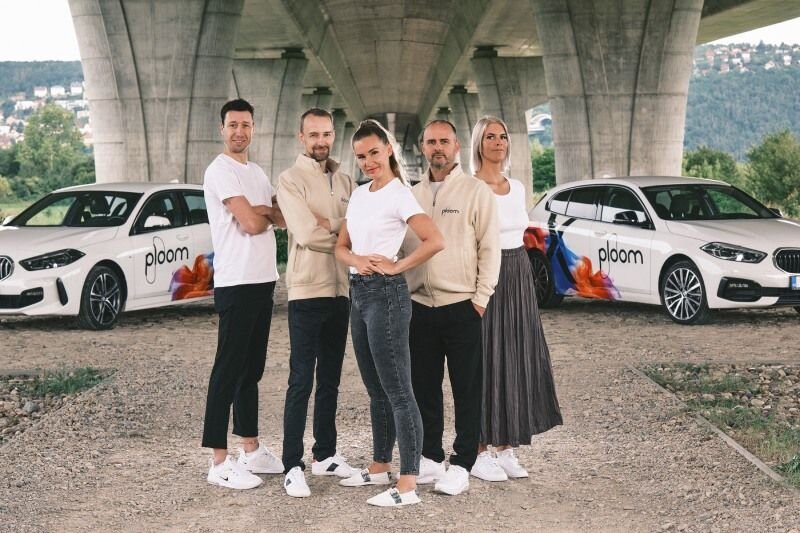 Pět lidí v merchi Ploom před dvěma branded auty pod mostem – týmová lifestyle fotografie Ploom.