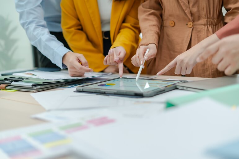 Mehrere Personen analysieren gemeinsam Daten und Diagramme auf einem Tablet und besprechen die Ergebnisse im Team.