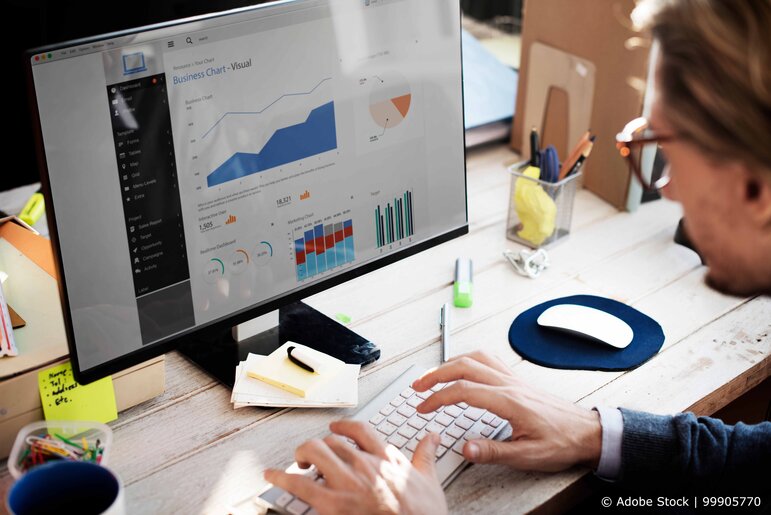 Eine Person arbeitet am Schreibtisch vor einem großen Monitor und analysiert übersichtliche Geschäftsdiagramme und Statistiken in einer modernen Arbeitsumgebung