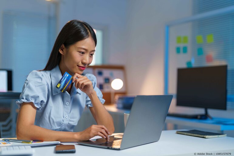 Eine Frau, die mit ihrer Kreditkarte in der Hand etwas am Laptop kauft.