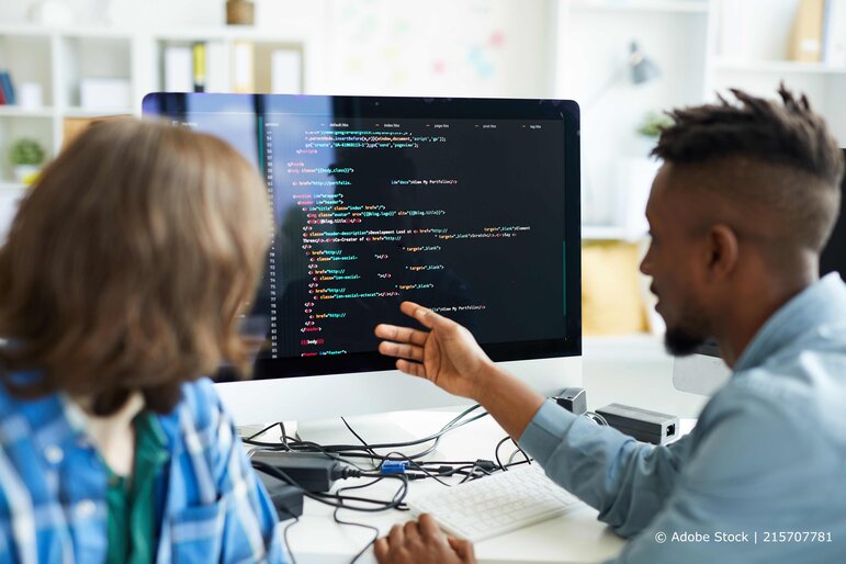 Zwei Softwareentwickler besprechen gemeinsam Programmcode auf einem großen Bildschirm in einer modernen Büroumgebung.