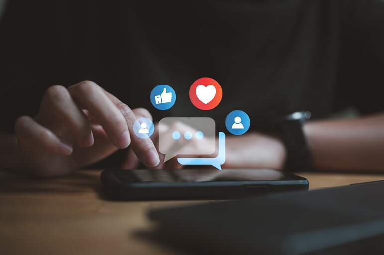 Eine Person nutzt ihr Smartphone für die Kommunikation in sozialen Medien, während Symbole für Likes, Kommentare und Interaktionen eingeblendet werden.