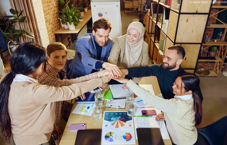Eine diverse Gruppe reicht sich im Büro die Hände