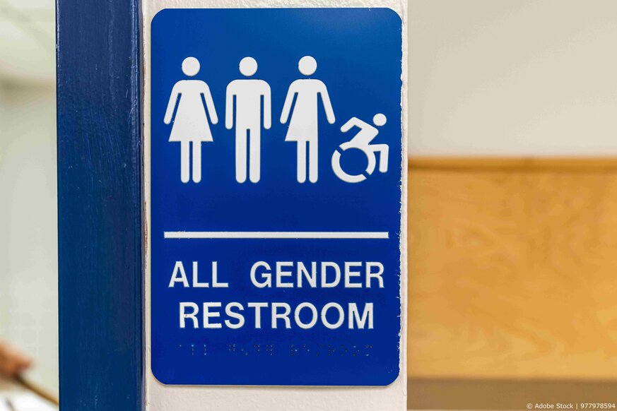 Blue and white all gender and accessible restroom sign with Braille code on a wall.