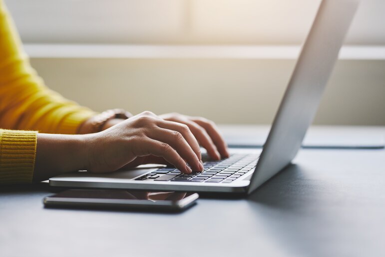 Person tippt auf einem Laptop in heller Arbeitsumgebung. Das Bild steht für digitales Arbeiten, Online Kommunikation und modernes Arbeiten am Computer.