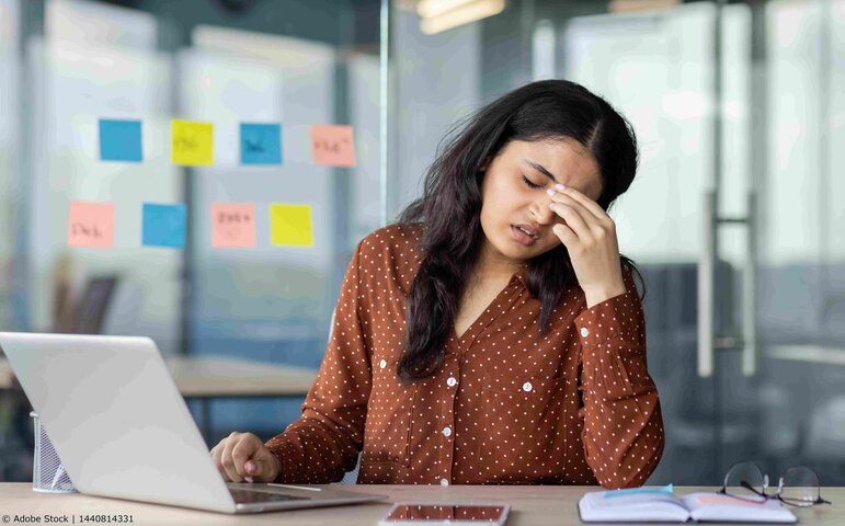 Eine müde Mitarbeiterin sitzt am Schreibtisch vor ihrem Laptop