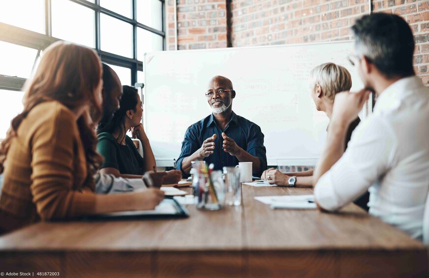 A diverse team sitting at a table together and talking to each other.