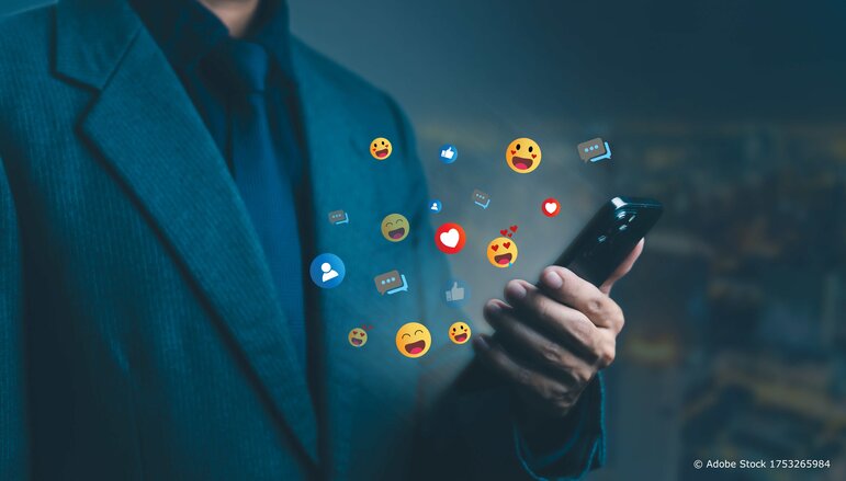 Ein Geschäftsmann nutzt ein Smartphone, während Social Media Reaktionssymbole wie Likes, Herzen und Emojis um ihn herum schweben.