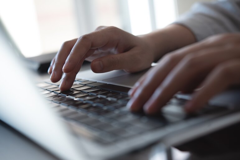 Nahaufnahme einer Person beim Tippen auf einem Laptop, begleitet vom digitalen Assistenten Selly für schnelle Unterstützung.