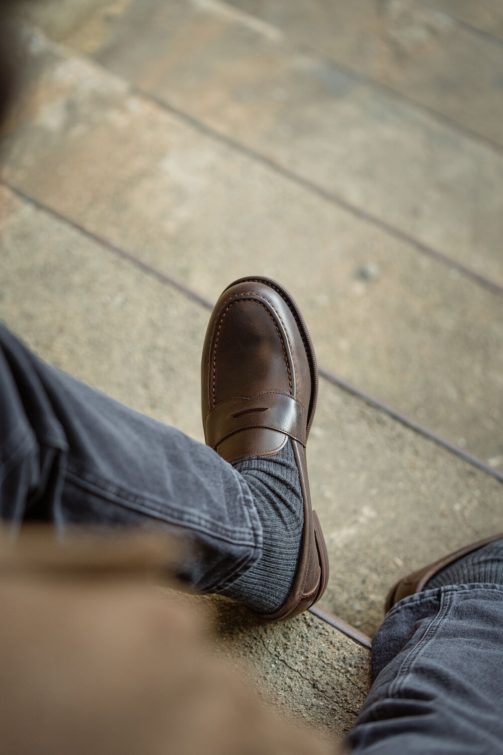 Person in grey jeans wearing waxy calf loafer, seated on a step.