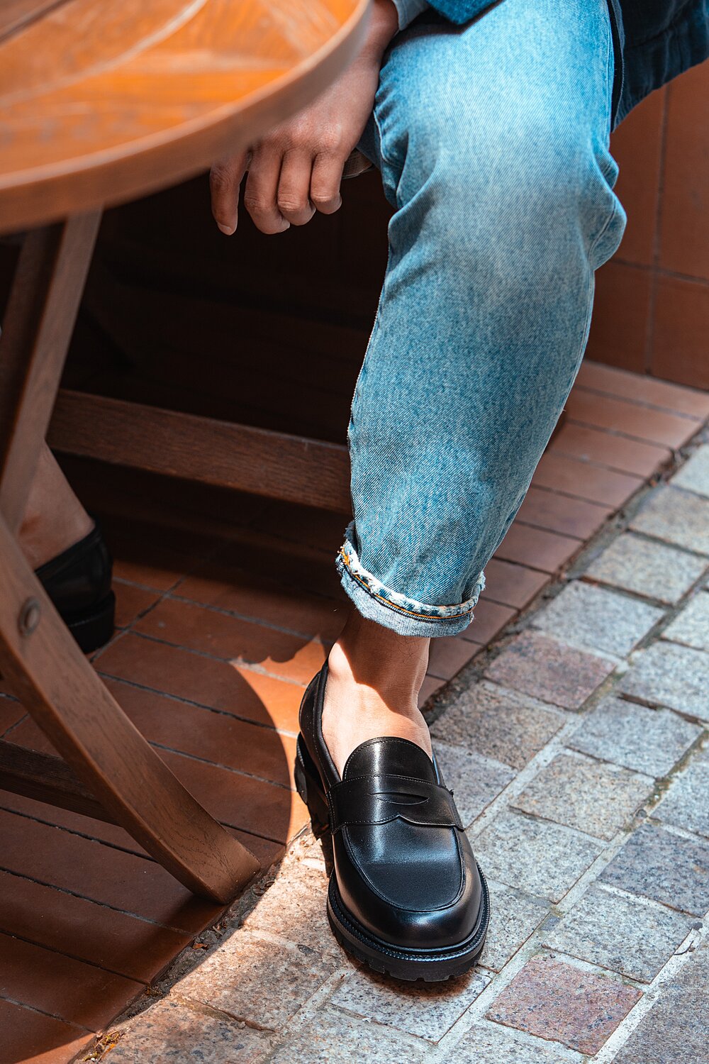 Person sitting wearing jeans & brown black leather loafers.