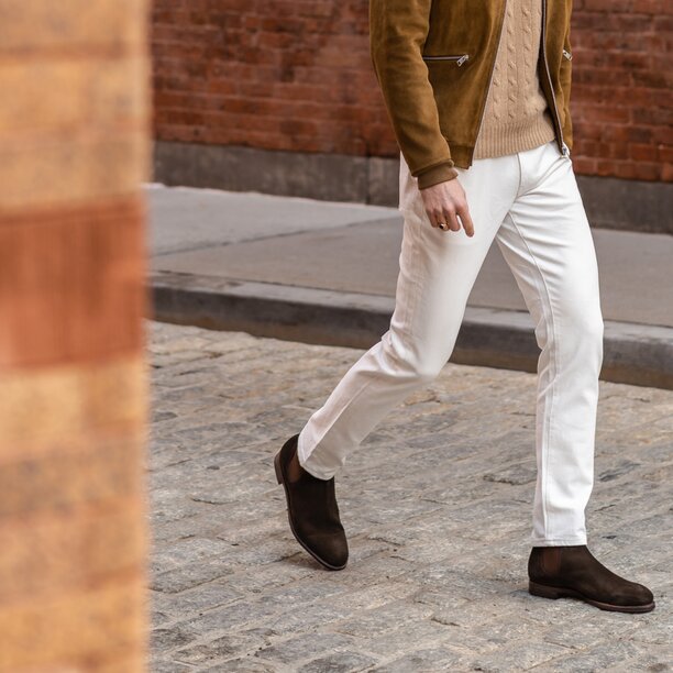 Person walking on street wearing brown suede chelsea boots