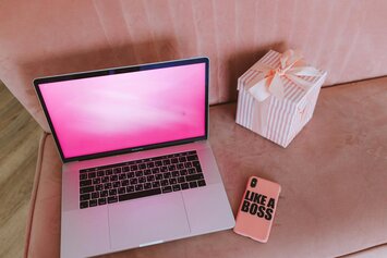 Laptop with pink screen and phone case that reads Like a Boss