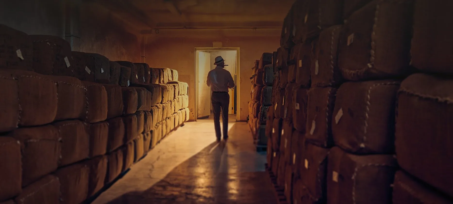 A storage room, the production facilities of Oettinegr Davidoff in the Dominican Republic. A man wearing a hat stands in a room full of boxes. 