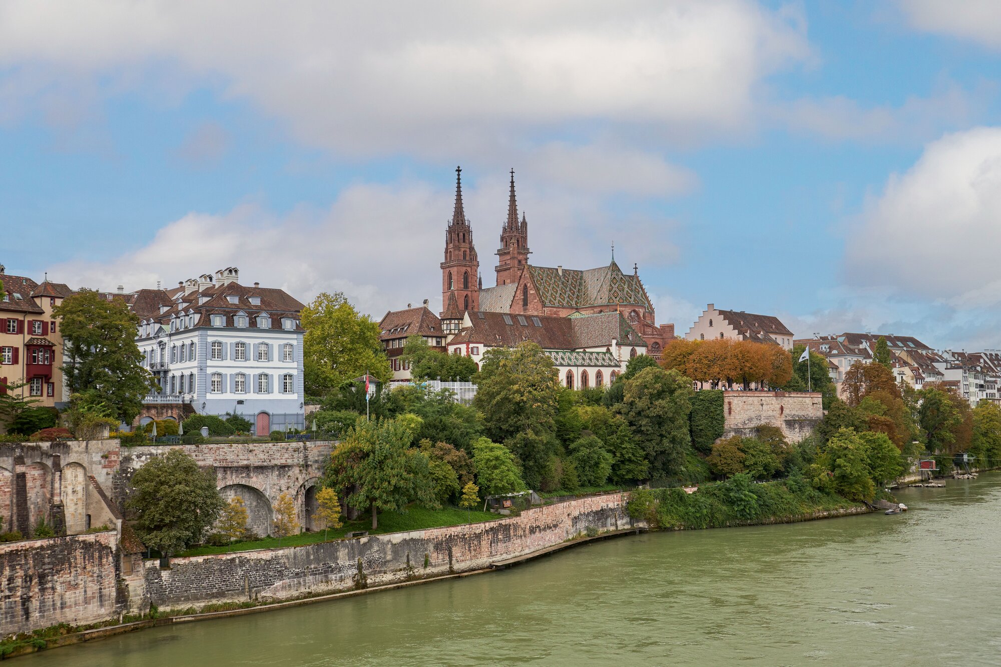 Stadtansicht von Basel, Schweiz, mit Blick auf das Basler Münster und den Rhein und die malerische Landschaft im Hintergrund.