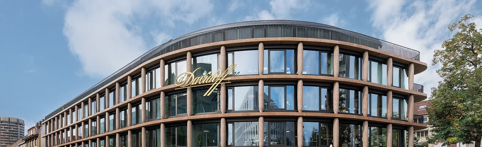 A modern glass building with an exterior facade featuring columns that resemble cigars. This is the Maison Davidoff building, serving as the headquarters in Basel.