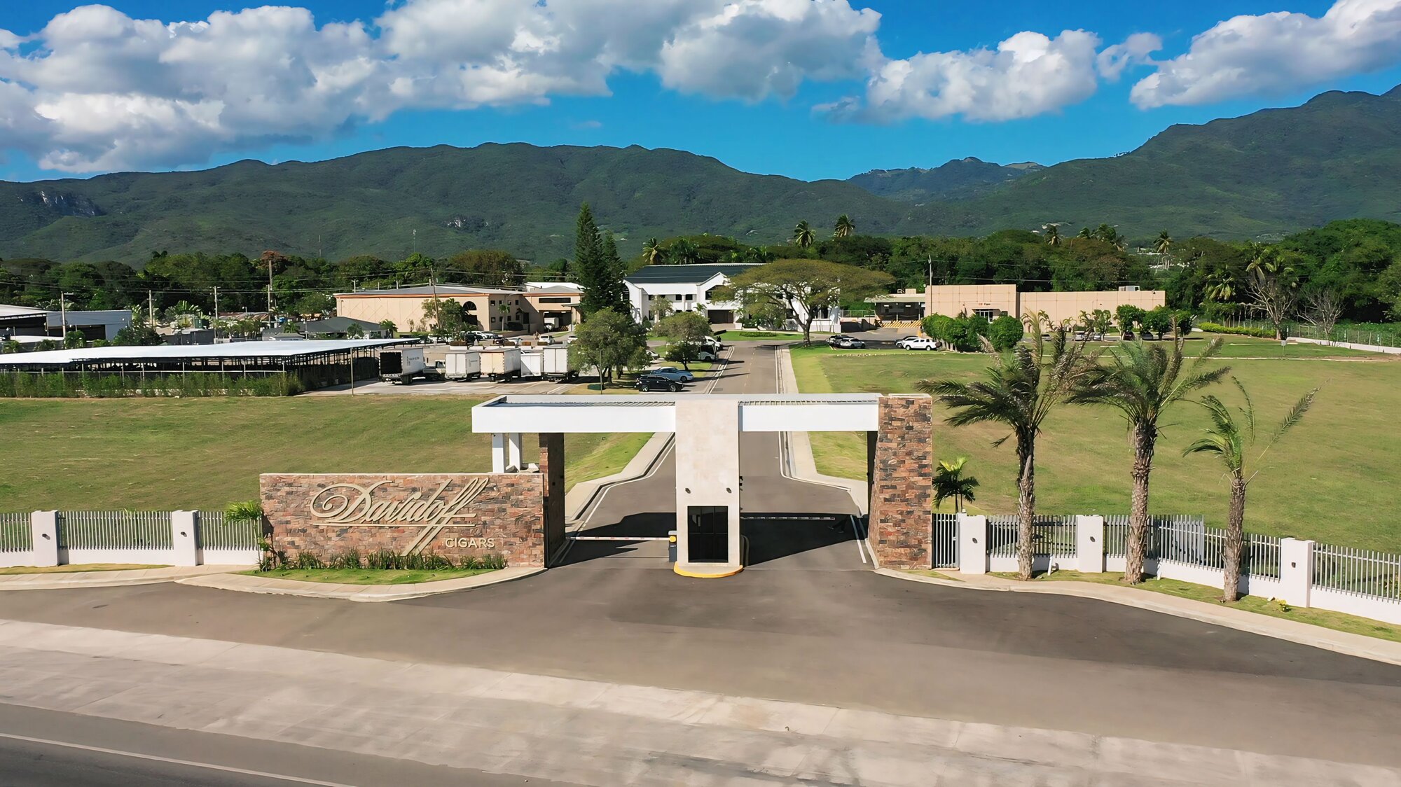 Exterior of the Davidoff manufacturing site in the Dominican Republi. A modern white building with palm trees and landscaped garden, featuring the Davidoff logo above the entrance.