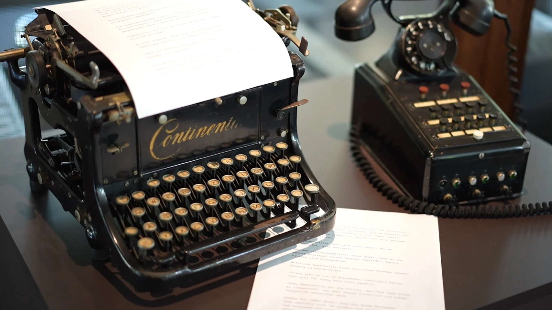 An antique typewriter with a sheet of paper and a vintage rotary phone display on a table, showcasing classic communication tools.