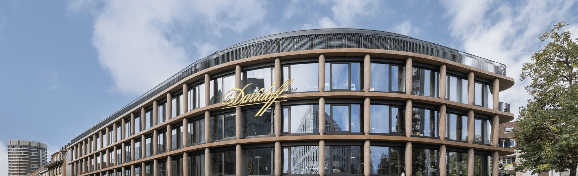 A modern glass building with an exterior facade featuring columns that resemble cigars. This is the Maison Davidoff building, serving as the headquarters in Basel.