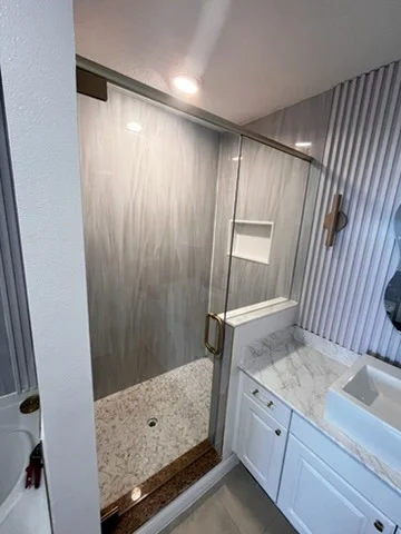 Sliding glass shower door with a gray tile surround and white vanity