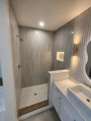 Walk-in glass shower beside a white vanity with textured wall tile