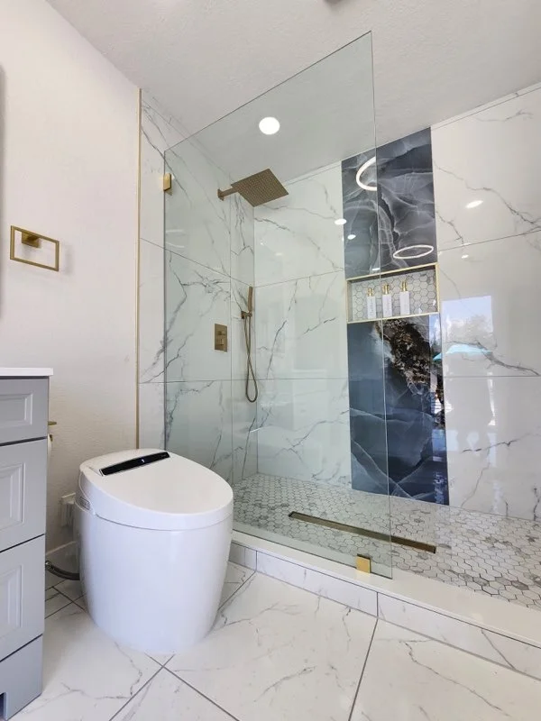 Frameless glass shower enclosure with brushed gold fixtures and marble tile