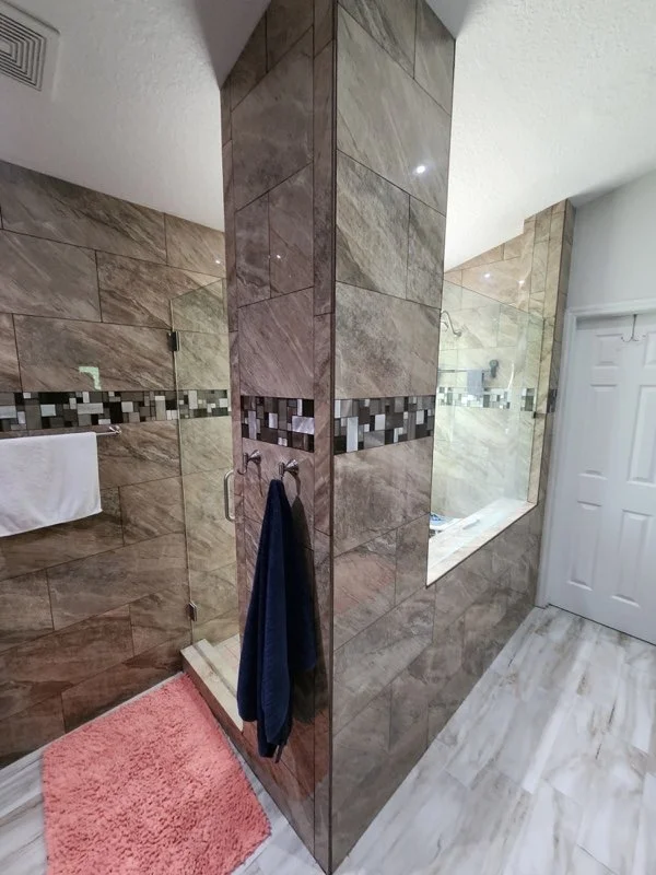 Glass shower door installed in a warm brown tiled bathroom
