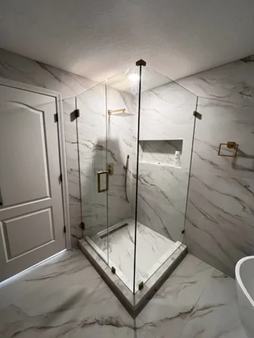 Corner frameless glass shower enclosure with black hardware and marble walls