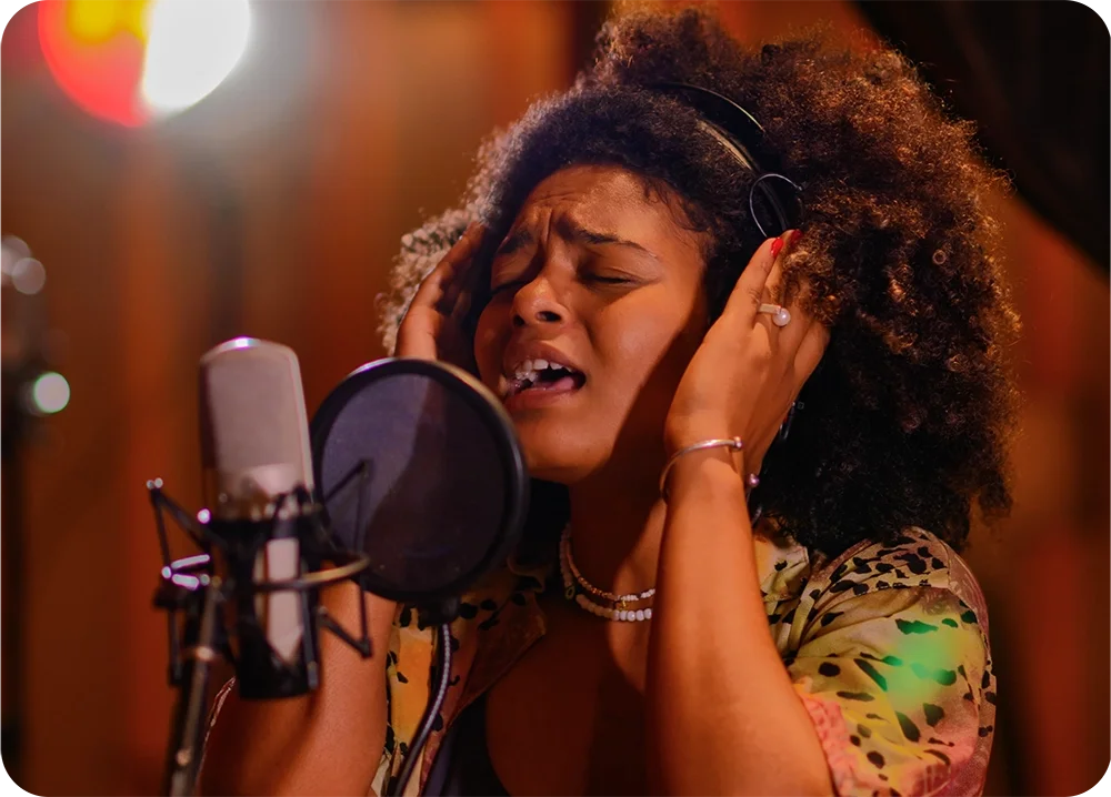 A female wearing headphones in the recording studio singing into a microphone with pop filter