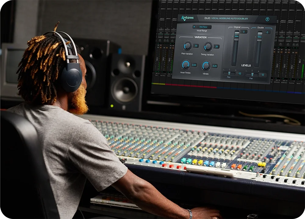 a man in a recording engineer room sitting at the mixer console using using Duo by AutoTune on the computer