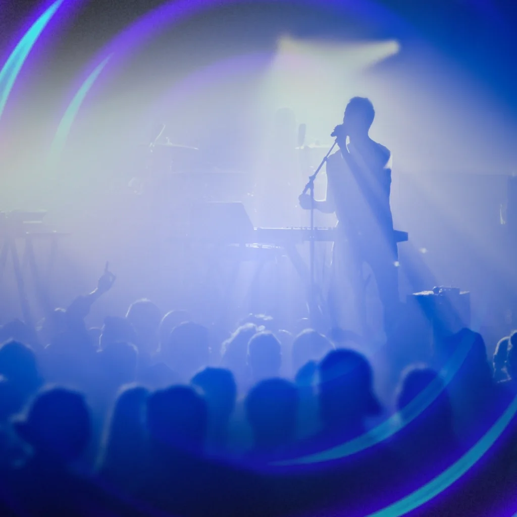 The silhouette of a man singing into a microphone while performing on stage in front of a crowd of people
