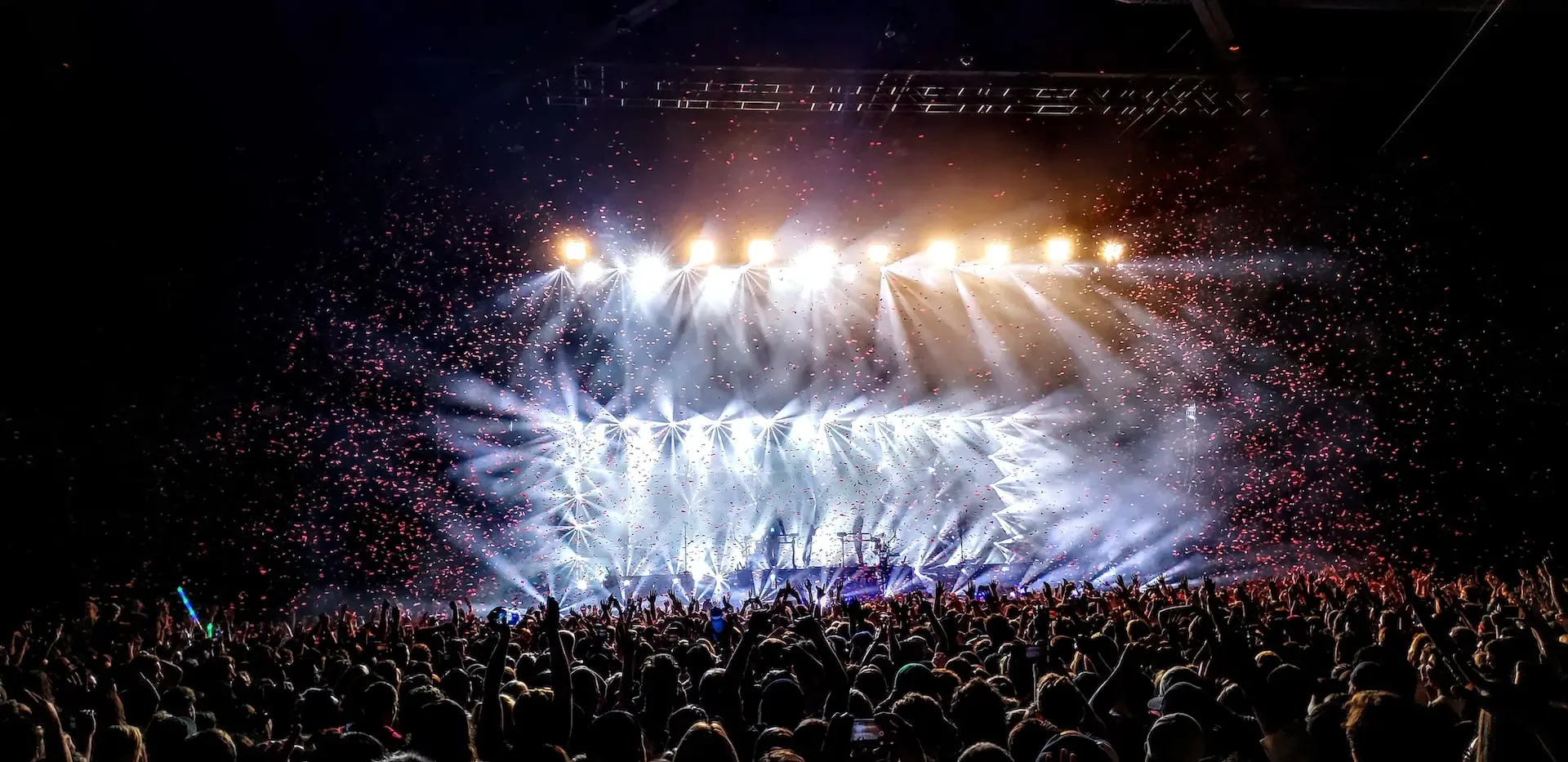 Lights flooding a stage with a huge crowd around it