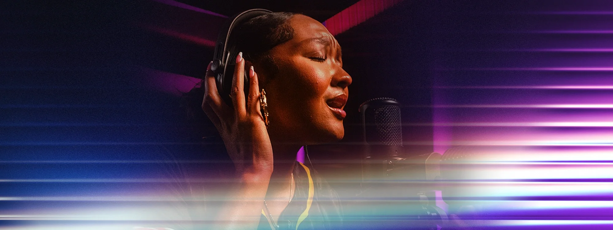 A woman holding her headphones to her ears while singing into a microphone