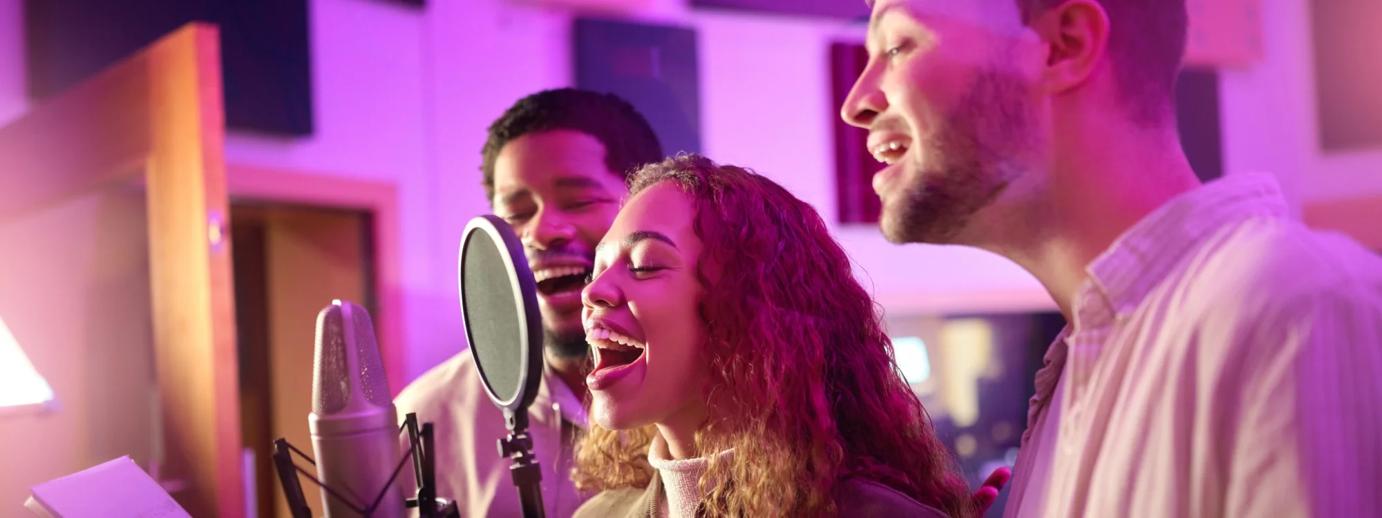 Two men and a woman singing into a studio microphone