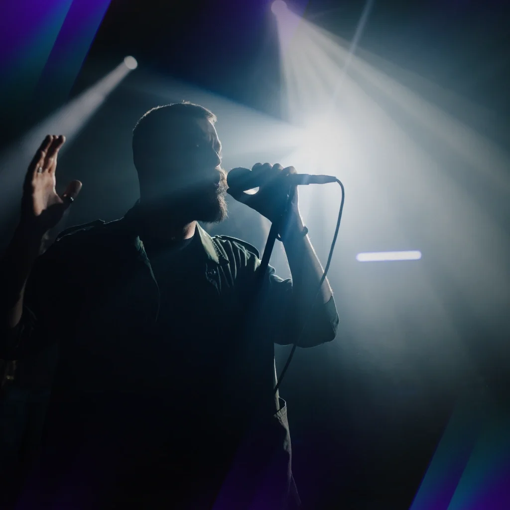 A man singing into a microphone with a spotlight on him