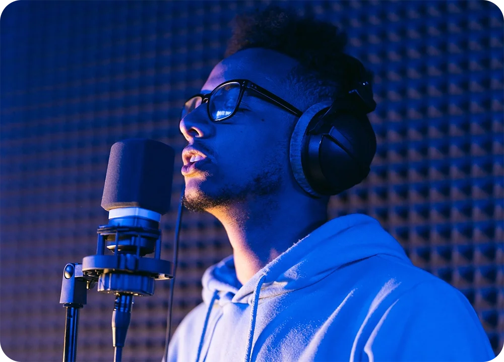 A man wearing headphones in a vocal booth singing into a microphone
