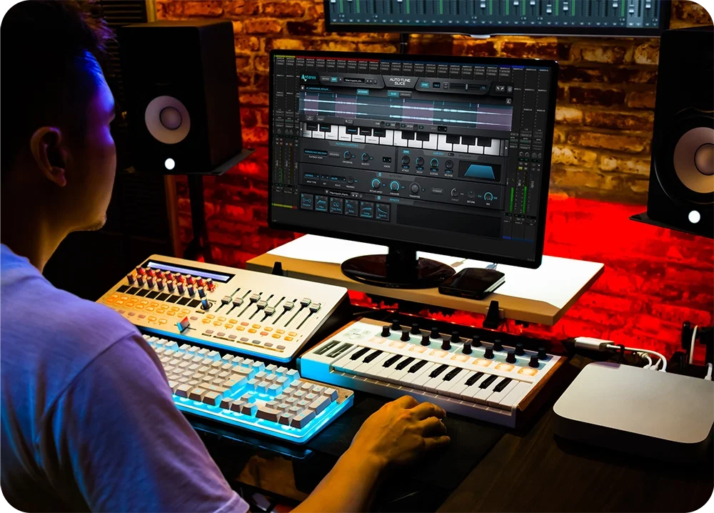A male in a recording studio working at a desk using Slice by AutoTune on the computer