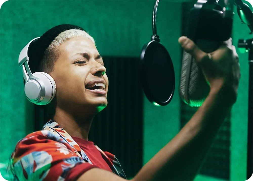 A man in the vocal booth wearing headphones and grabbing a microphone while singing into it