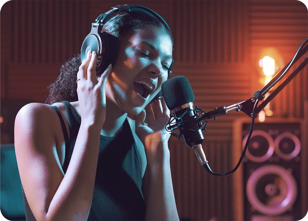 A female in recording studio wearing headphones and singing into a microphone