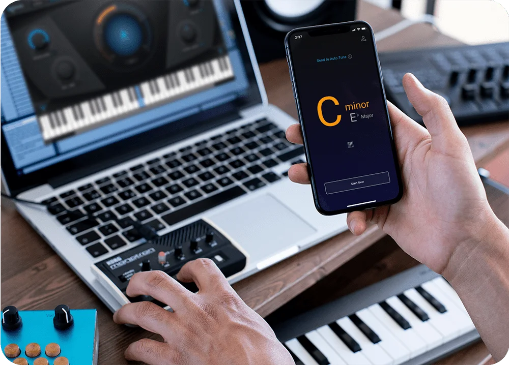 Detail shot of home recording studio desk with hands in front of a computer holding an iPhone with AutoKey Mobile on it
