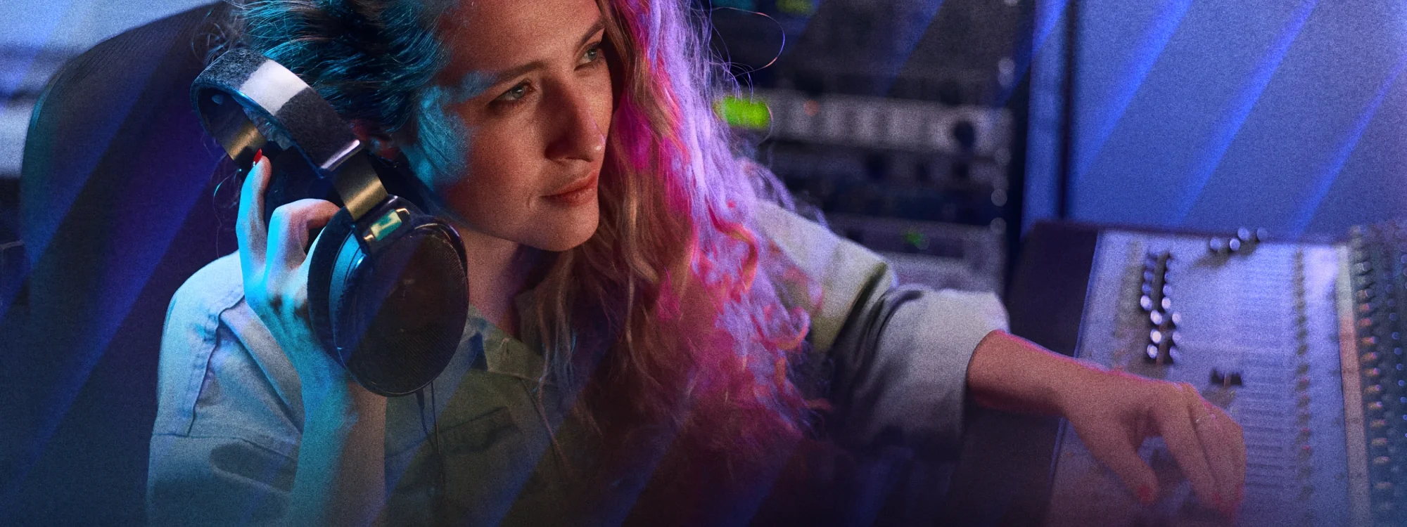 A woman holding headphones up to her ear as she adjusts levels on a mixing console