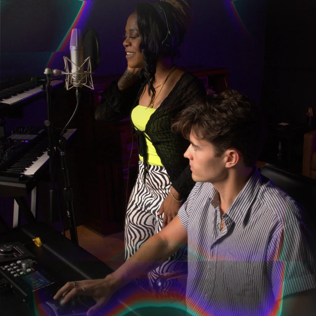 A woman standing up and singing into a microphone with a man sitting down next to her