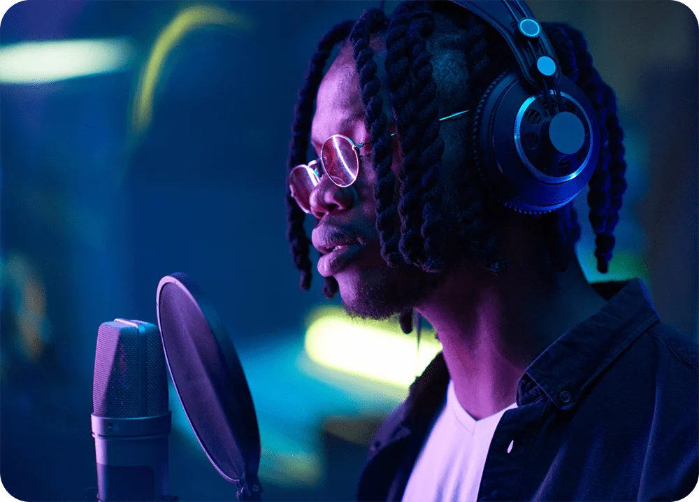 A man in a vocal booth wearing headphones and singing into a microphone