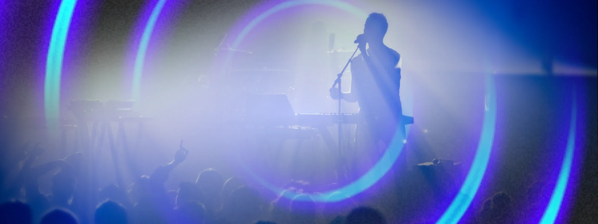The silhouette of a man singing into a microphone while performing on stage in front of a crowd of people