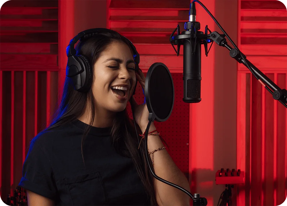 female in vocal booth singing into a microphone with pop-filter