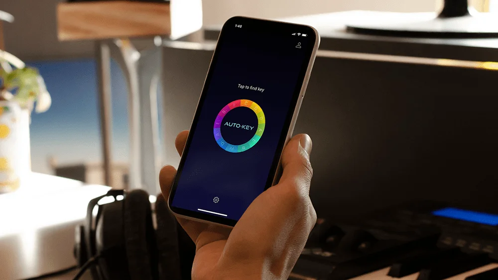 A hand holding an iPhone with AutoKey Mobile by AutoTune on it in home music studio